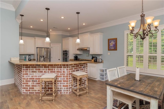 kitchen featuring hardwood / wood-style floors, stainless steel appliances, hanging light fixtures, ornamental molding, and a breakfast bar