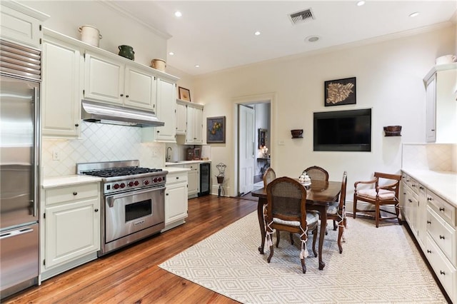 kitchen with white cabinets, light hardwood / wood-style flooring, sink, premium appliances, and decorative backsplash