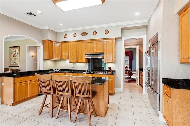 kitchen featuring a kitchen breakfast bar, built in fridge, a center island, and light tile floors