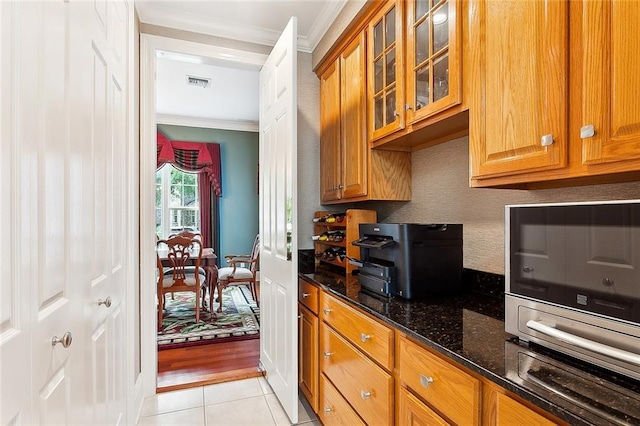 kitchen with crown molding, light tile flooring, and dark stone countertops