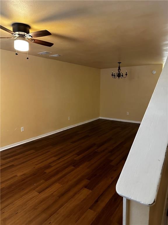 empty room featuring ceiling fan with notable chandelier and dark hardwood / wood-style flooring