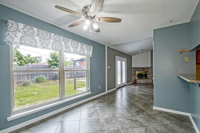 unfurnished living room featuring a healthy amount of sunlight, a fireplace, ceiling fan, and tile floors