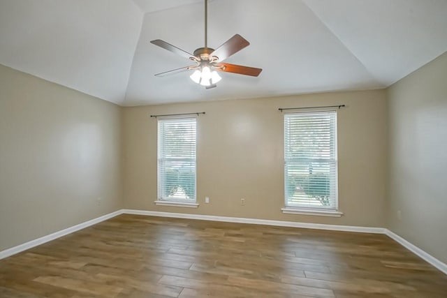 empty room with a wealth of natural light, wood-type flooring, ceiling fan, and vaulted ceiling