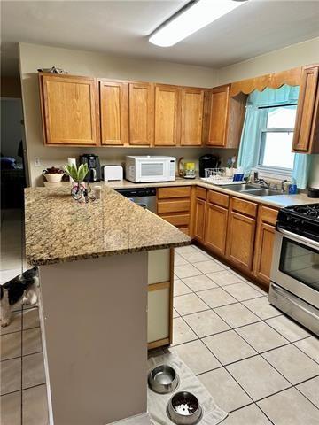 kitchen with kitchen peninsula, gas range, light stone countertops, sink, and light tile floors