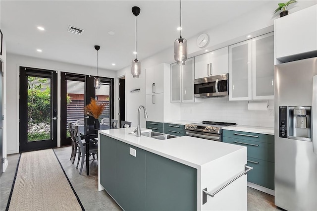 kitchen with appliances with stainless steel finishes, white cabinets, backsplash, hanging light fixtures, and a center island with sink