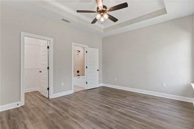 unfurnished bedroom with a closet, a tray ceiling, ceiling fan, a walk in closet, and hardwood / wood-style flooring