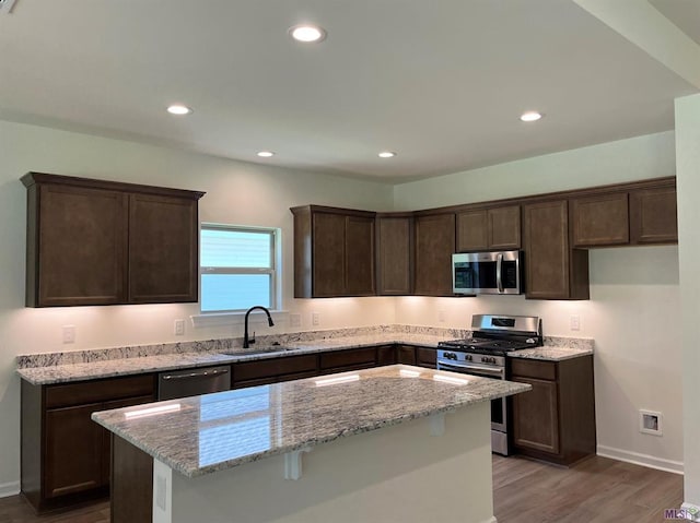 kitchen with a kitchen island, light stone countertops, stainless steel appliances, and hardwood / wood-style floors