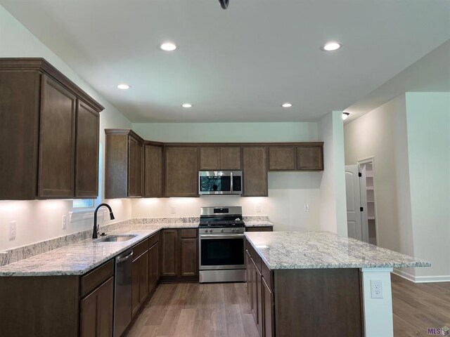 kitchen with wood-type flooring, a kitchen island, appliances with stainless steel finishes, and sink