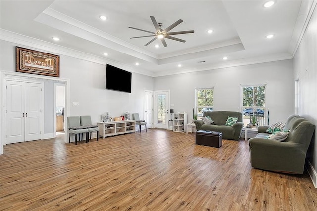 living room with ceiling fan, a tray ceiling, and wood-type flooring