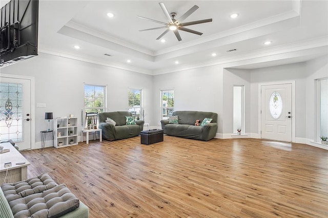 living room with ceiling fan, plenty of natural light, light wood-type flooring, and a raised ceiling