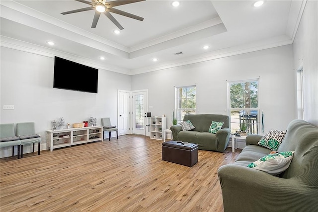 living room with ornamental molding, light wood-type flooring, a tray ceiling, a high ceiling, and ceiling fan