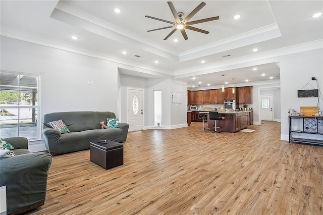 living room featuring a tray ceiling, light wood-type flooring, and crown molding