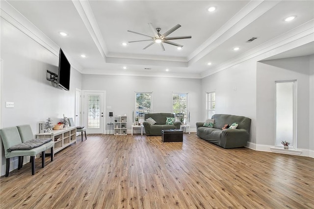 living room with ceiling fan, a raised ceiling, ornamental molding, and wood-type flooring