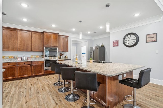 kitchen featuring light hardwood / wood-style floors, hanging light fixtures, a kitchen island with sink, and stainless steel appliances