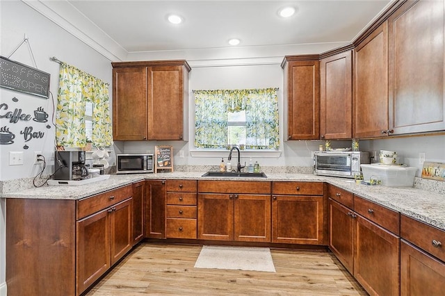 kitchen with crown molding, sink, light wood-type flooring, and light stone counters