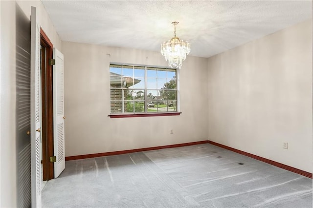 carpeted spare room with a textured ceiling and an inviting chandelier