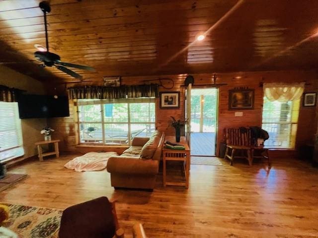 living room featuring ceiling fan, vaulted ceiling, wood-type flooring, wood walls, and wooden ceiling