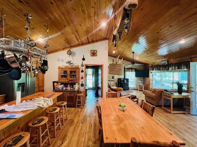 dining area featuring light hardwood / wood-style flooring, a wood stove, wood ceiling, ceiling fan, and vaulted ceiling