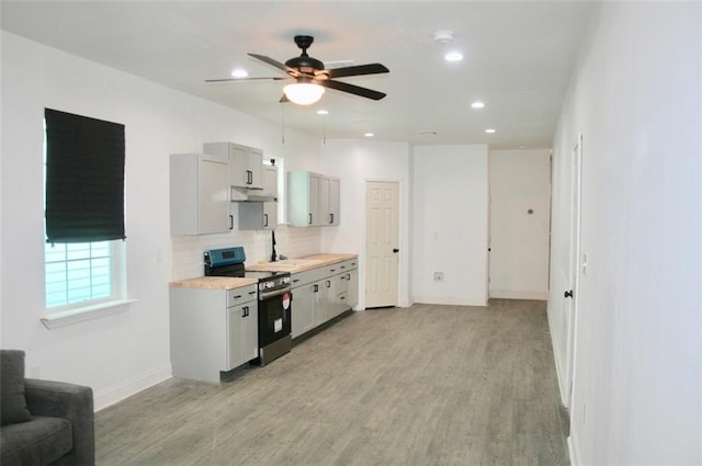 kitchen featuring backsplash, ceiling fan, light wood-type flooring, and stainless steel electric range