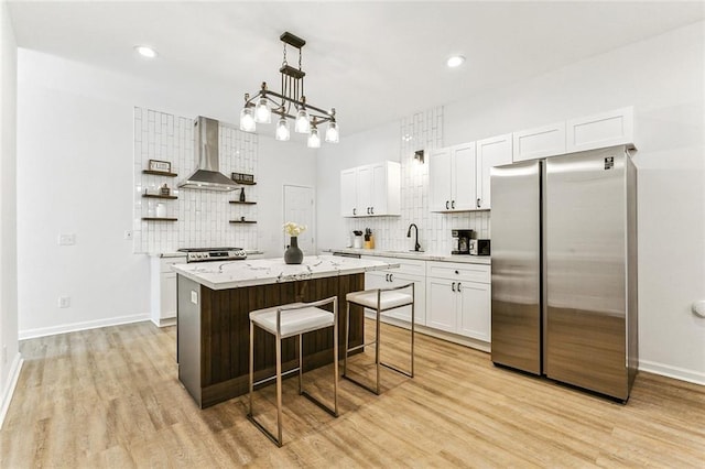 kitchen with appliances with stainless steel finishes, a center island, white cabinetry, and wall chimney exhaust hood