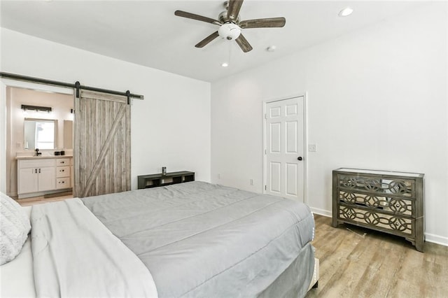 bedroom with a barn door, ensuite bathroom, ceiling fan, and light hardwood / wood-style floors