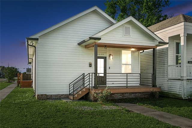 back house at dusk with a lawn and covered porch