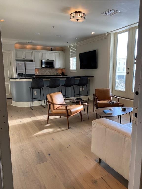 living room featuring a healthy amount of sunlight, light hardwood / wood-style floors, and crown molding