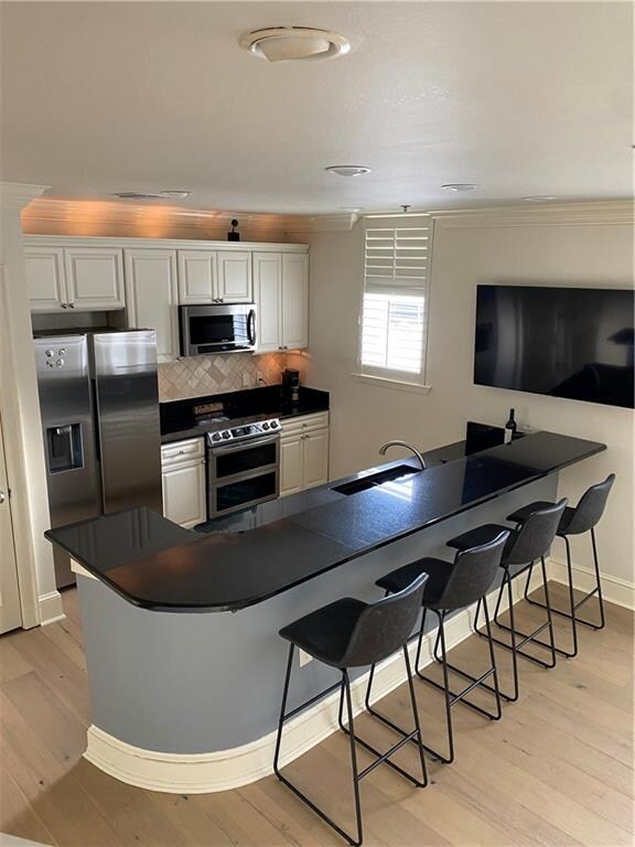 kitchen with appliances with stainless steel finishes, a breakfast bar area, light hardwood / wood-style flooring, sink, and backsplash