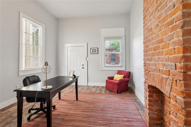 office featuring brick wall, wood-type flooring, and a fireplace