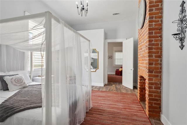 bedroom with an inviting chandelier, brick wall, and wood-type flooring