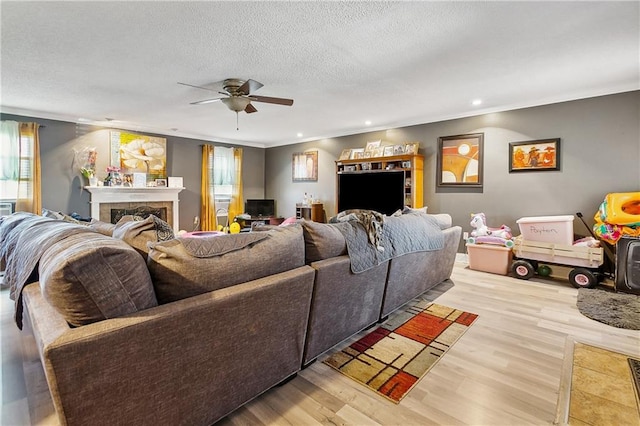 living room featuring ceiling fan, light hardwood / wood-style flooring, a textured ceiling, and a tile fireplace