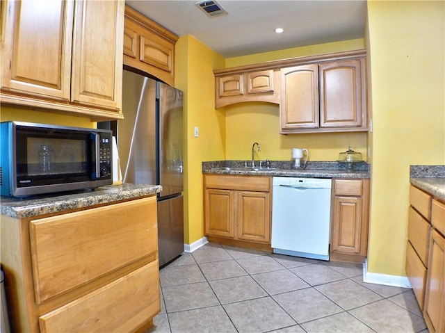 kitchen featuring sink, light tile patterned flooring, dark stone counters, and appliances with stainless steel finishes