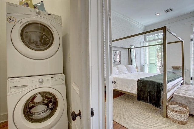 laundry room featuring hardwood / wood-style flooring, ornamental molding, and stacked washer and dryer