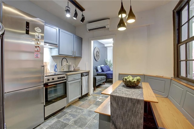 kitchen featuring decorative light fixtures, stainless steel appliances, a wall unit AC, track lighting, and sink