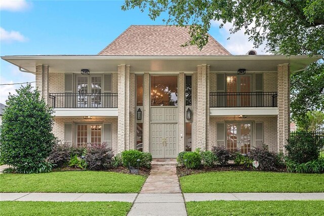 view of front facade with a balcony, french doors, and a front lawn