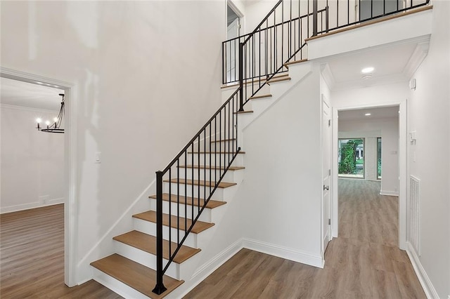 stairs with a notable chandelier, crown molding, and hardwood / wood-style floors