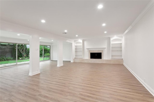 unfurnished living room featuring ornamental molding, a fireplace, built in shelves, light hardwood / wood-style floors, and ceiling fan