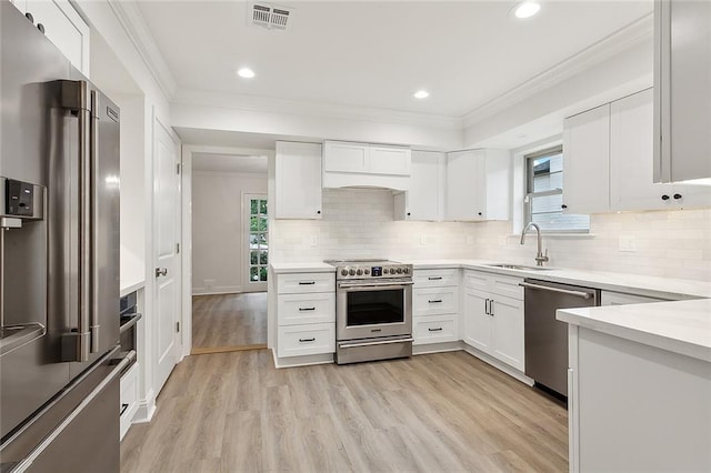 kitchen featuring backsplash, light hardwood / wood-style floors, custom exhaust hood, white cabinets, and premium appliances