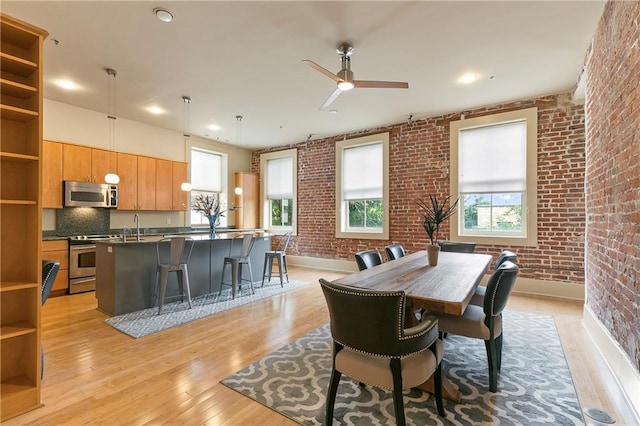 dining area featuring brick wall, ceiling fan, and light hardwood / wood-style flooring