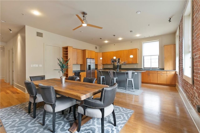 dining space with brick wall, ceiling fan, and light hardwood / wood-style flooring