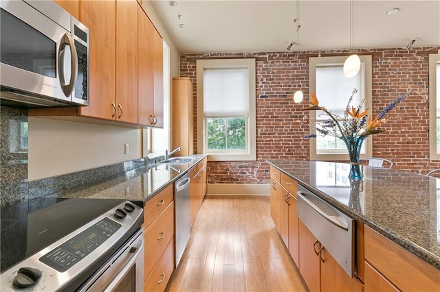 kitchen with brick wall, dark stone counters, light hardwood / wood-style floors, appliances with stainless steel finishes, and pendant lighting