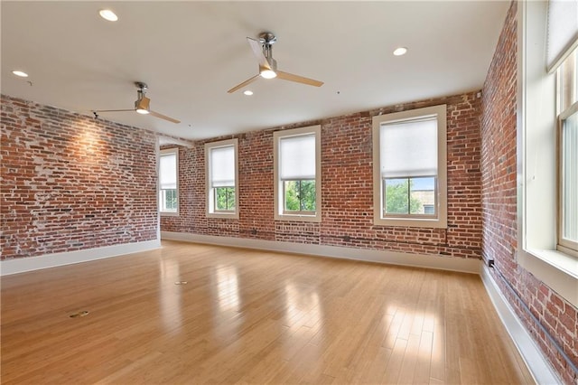 unfurnished room with brick wall, ceiling fan, and light hardwood / wood-style flooring