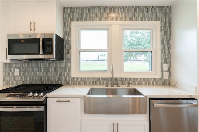 kitchen featuring white cabinets, light stone counters, backsplash, appliances with stainless steel finishes, and sink