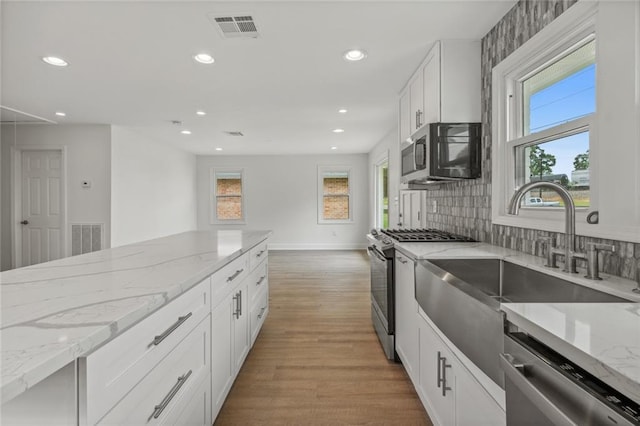 kitchen with light stone counters, stainless steel appliances, backsplash, white cabinetry, and wood-type flooring