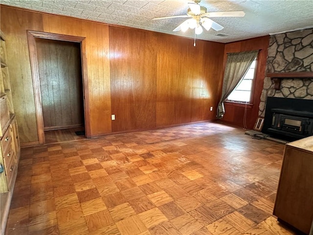 unfurnished living room featuring wood walls, a stone fireplace, and ceiling fan