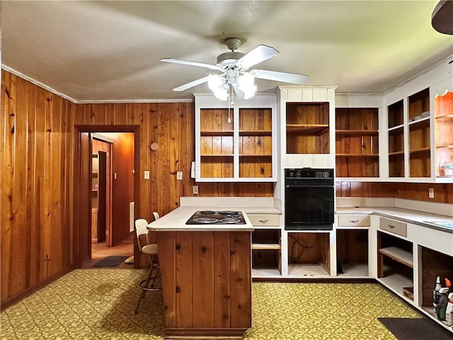 kitchen with wood walls, black oven, ceiling fan, and light tile floors