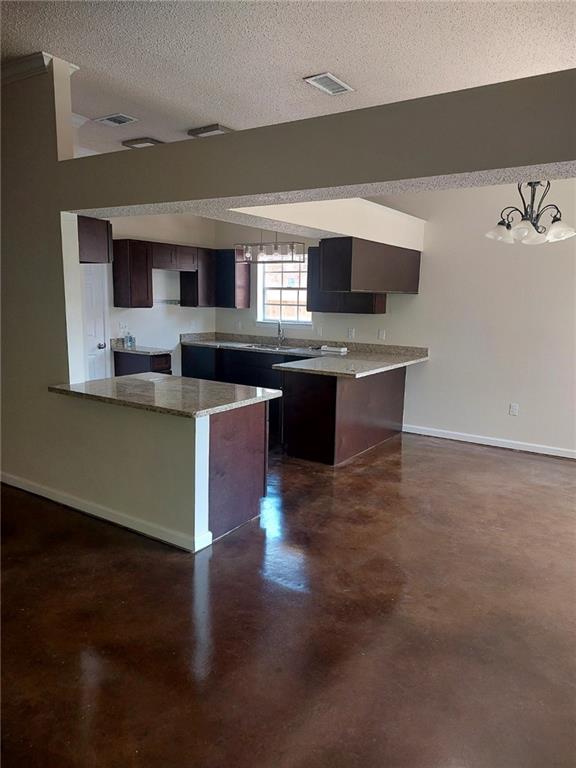 kitchen with decorative light fixtures, a center island, light stone countertops, dark brown cabinets, and a textured ceiling