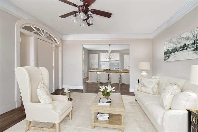 living room with ceiling fan with notable chandelier, crown molding, baseboards, and wood finished floors