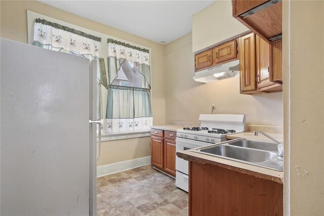 kitchen with white appliances, brown cabinetry, baseboards, light countertops, and under cabinet range hood