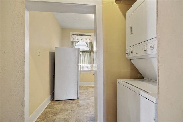 clothes washing area featuring laundry area, stacked washer and clothes dryer, and baseboards